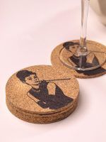 A neat stack of Glimpse Homes 4-inch cork coasters featuring a retro Audrey Hepburn design, positioned near a stemmed glass.