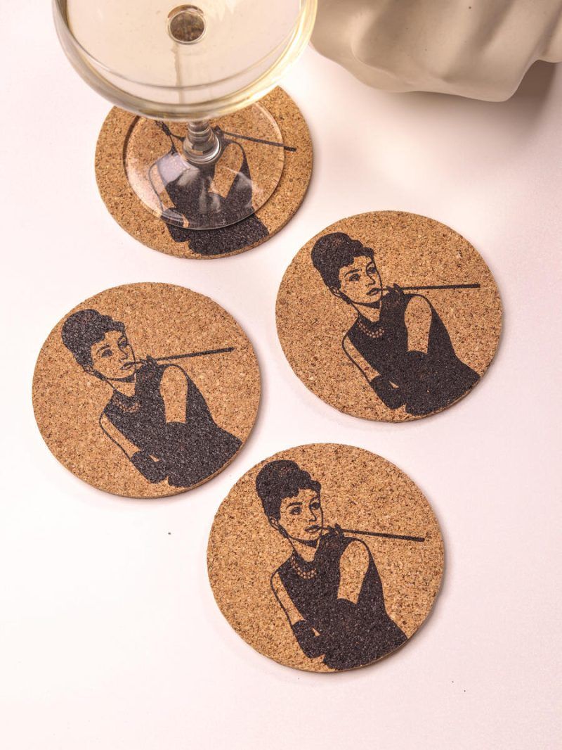 Top view of four Glimpse Homes 4-inch Audrey Hepburn cork coasters stylishly scattered around a cocktail glass on a light background.