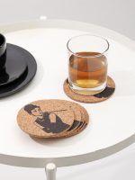 A stacked set of Glimpse Homes 4-inch Audrey Hepburn cork coasters alongside a drinking glass on a modern white side table.