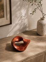 The Trinity Knot wooden sculpture displayed on a wooden console table next to a rustic vase, showing how the abstract decor adds an earthy aesthetic to a living room.