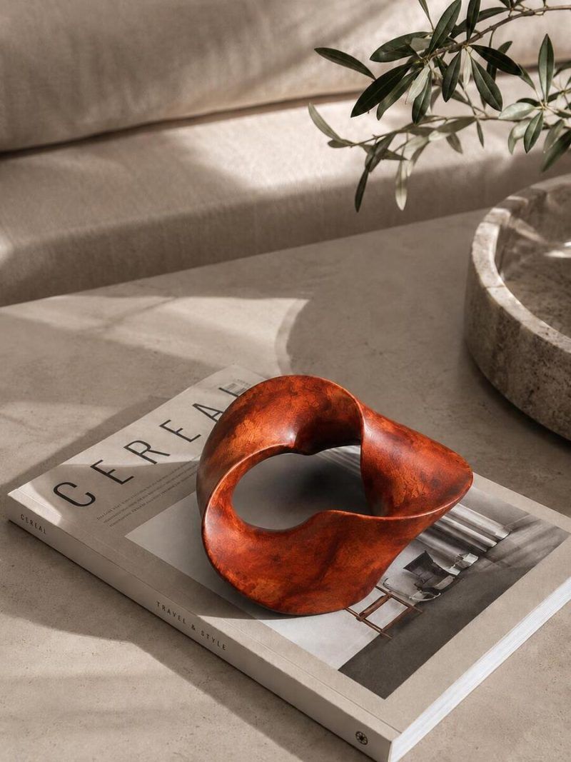 The Trinity Knot abstract wooden centrepiece styled on top of a Cereal magazine on a modern coffee table, highlighting its rich mahogany brown teakwood finish.