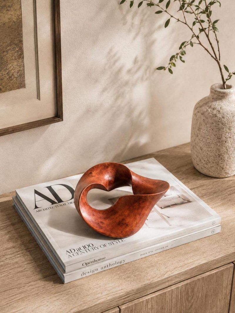 Premium wooden knot decor styled on a stack of Architectural Digest magazines on a wooden cabinet, showcasing The Trinity Knot by Glimpse Homes as a sophisticated interior accent.