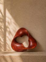 The Trinity Knot abstract wooden shelf decor standing upright on a stone ledge, demonstrating the spiritual, Zen-like balance of the continuous teakwood loop.