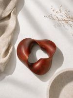 Top view of The Trinity Knot by Glimpse Homes, an abstract wooden centrepiece in a matte mahogany brown finish resting on a textured white surface.