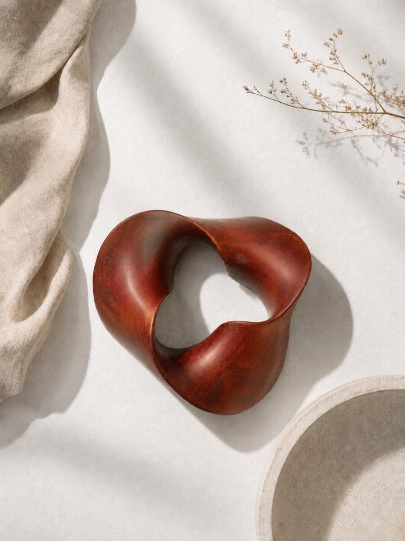 Top view of The Trinity Knot by Glimpse Homes, an abstract wooden centrepiece in a matte mahogany brown finish resting on a textured white surface.