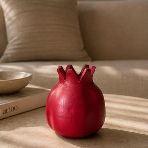 A ravishing red handmade terracotta pomegranate showpiece by Glimpse Homes, styled on a modern coffee table in a cozy living room setting.