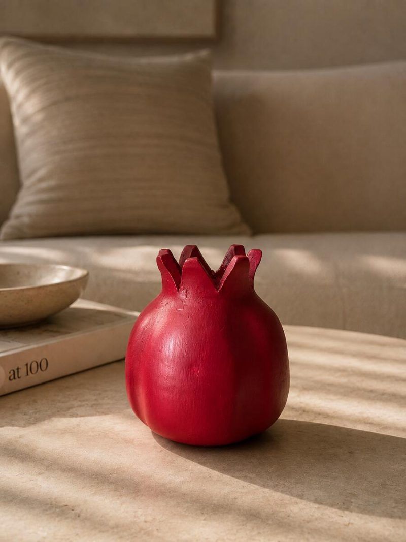 A ravishing red handmade terracotta pomegranate showpiece by Glimpse Homes, styled on a modern coffee table in a cozy living room setting.