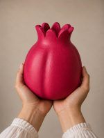 Two hands holding the large 7.5-inch ravishing red handmade terracotta pomegranate showpiece by Glimpse Homes, highlighting its substantial artisanal scale.