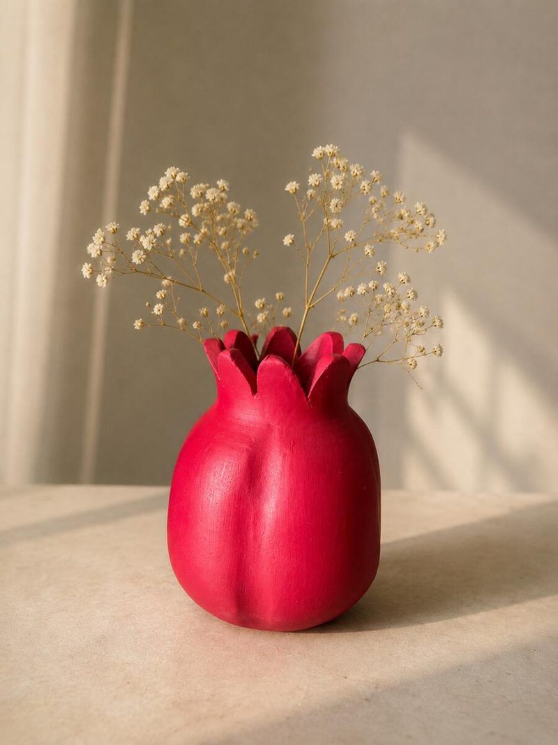 The large 7.5-inch ravishing red terracotta pomegranate showpiece styled creatively as a rustic vase with dry baby's breath flowers on a sunlit table.