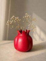 The ravishing red terracotta pomegranate showpiece styled as a rustic vase holding dry baby's breath flowers on a sunlit table.