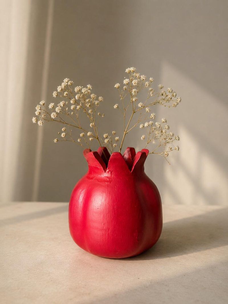 The ravishing red terracotta pomegranate showpiece styled as a rustic vase holding dry baby's breath flowers on a sunlit table.