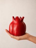 A person holding the ravishing red handmade terracotta pomegranate showpiece by Glimpse Homes in their palm to display its artisanal scale and semi-matte texture.