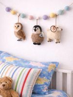 Glimpse Homes felt animal garland featuring a ram, owl, and penguin hanging above a child's bed with pastel pom-poms.