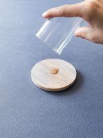 Hand pouring water from a glass onto a Glimpse Homes natural sandstone coaster, showing how it instantly absorbs the spill