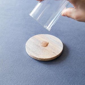 Hand pouring water from a glass onto a Glimpse Homes natural sandstone coaster, showing how it instantly absorbs the spill
