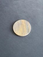 Glimpse Homes natural sandstone coaster on a grey surface, showing its round shape and earthy multi-tone veining pattern