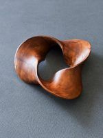 Glimpse Homes Trinity Wooden Knot decor sculpture in mahogany brown, showing its smooth tri-lobed twisted design on a grey surface.