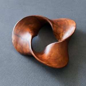 Glimpse Homes Trinity Wooden Knot decor sculpture in mahogany brown, showing its smooth tri-lobed twisted design on a grey surface.