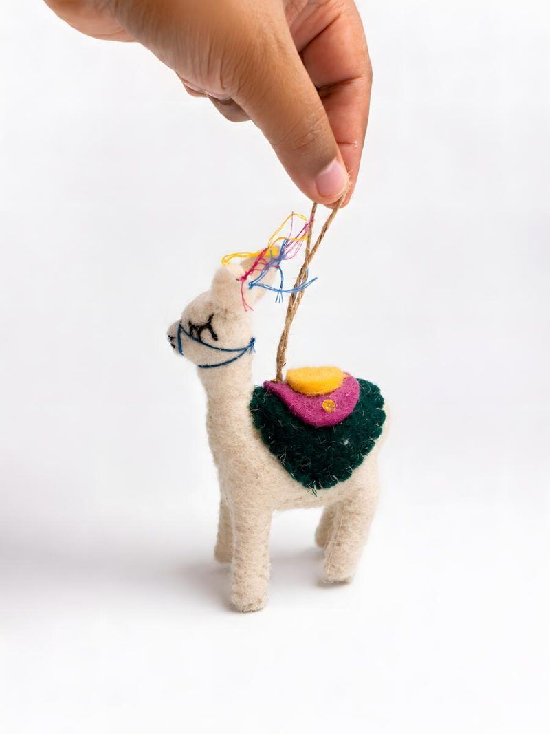 Hand holding a Glimpse Homes felt llama ornament showing colorful saddle and tassel detailing