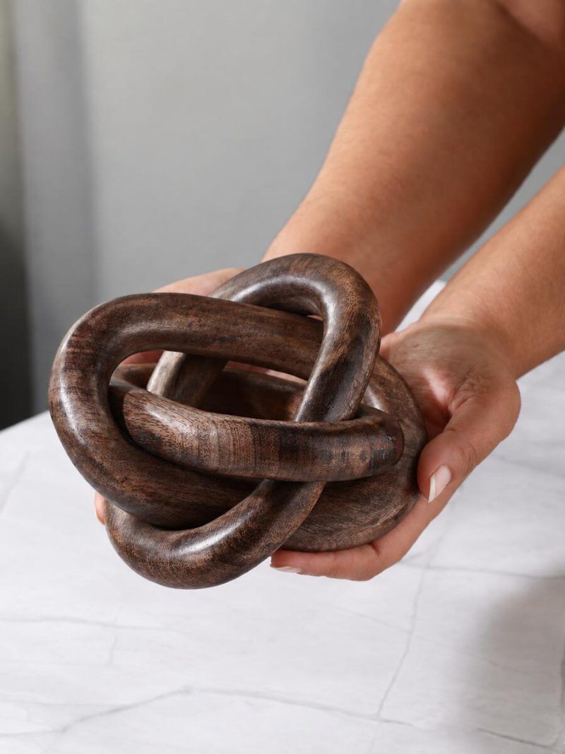 Hands holding Glimpse Homes 3 knot wooden chain sculpture in walnut finish showing texture detail