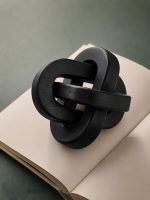 Black wooden triple knot decorative accent by Glimpse Homes placed on open book, close-up view.