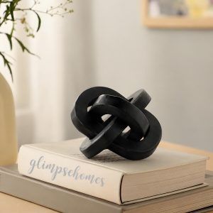 Black wooden triple knot sculpture by Glimpse Homes styled on stacked books for home decor.