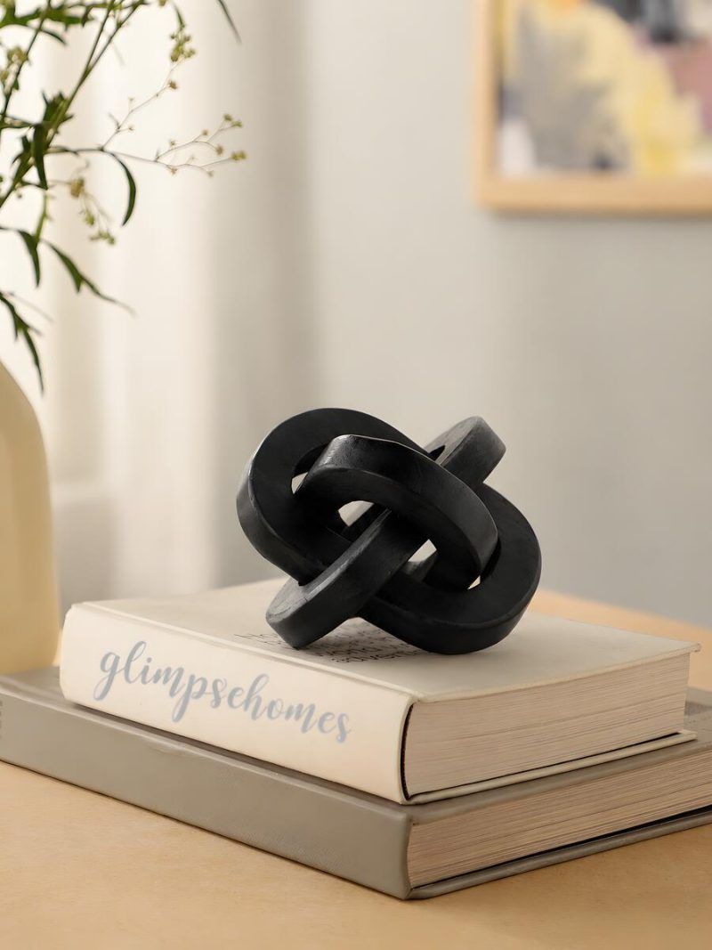 Black wooden triple knot sculpture by Glimpse Homes styled on stacked books for home decor.