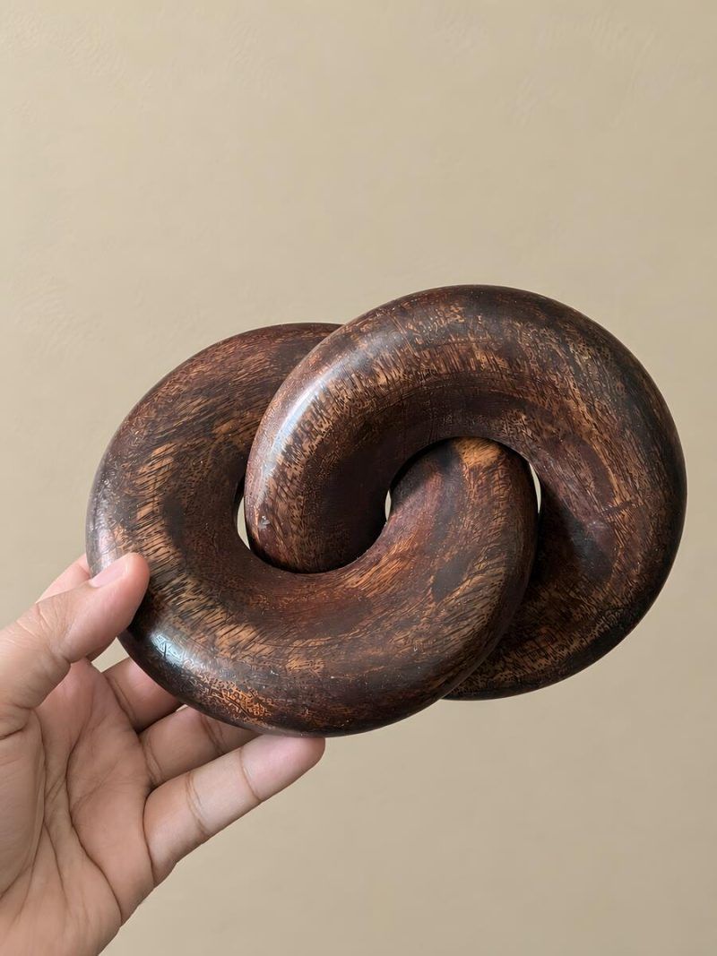 Hand holding Glimpse Homes walnut wooden knot chain decor to show size and scale.