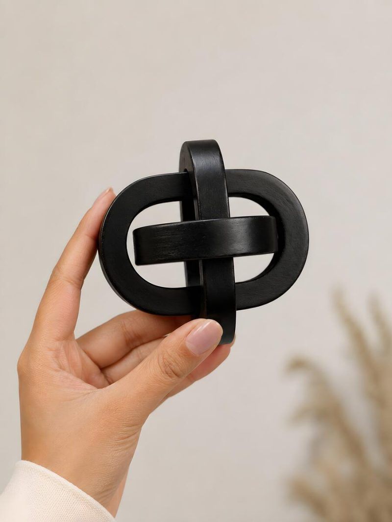 Hand holding Glimpse Homes small black wooden triple knot accent piece showing compact size.