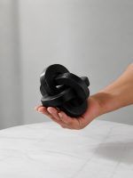 Glimpse Homes small black wooden triple knot piece resting in palm above marble side table.